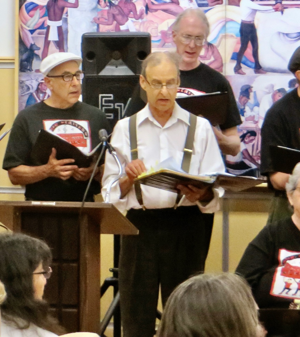 Four singers in a larger chorus,singing.